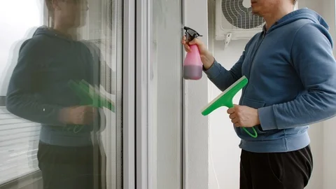 SIDE VIEW: Portrait of man sprays window cleaner on window and washes it Stock Footage 105888157