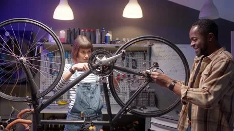 Side-view portrait of two attractive focused happy mechanics fixing bike gears Stock Footage 232868437
