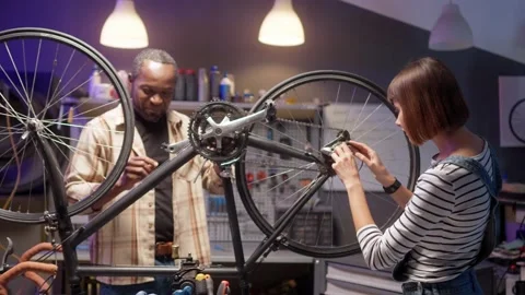 Side-view portrait of two skillful happy young mechanics fixing bike wheel Stock Footage 232868227