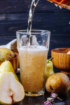Side view of pouring pear lemonade into a glass at dark background Stock Photos