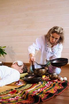 Side view of a practitioner using a red mallet and singing bowl beside a relaxed Stock Photos