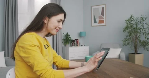 Side view of pretty cheerful young female scrolling and browsing on tablet while Stock Footage 134718109