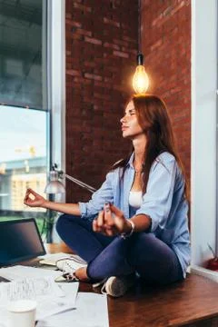 Side view of pretty creative female freelancer sitting in lotus pose on working Stock Photos