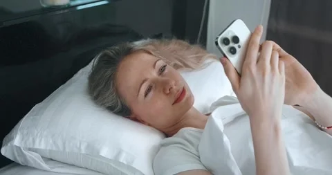Side view of pretty young caucasian woman lying in bed and using mobile phone Stock Footage 243422569