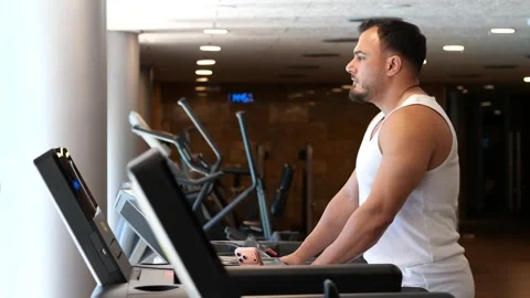 Side view profile of an athletic man walking on a treadmill in a modern gym.. Vidéo 344048935