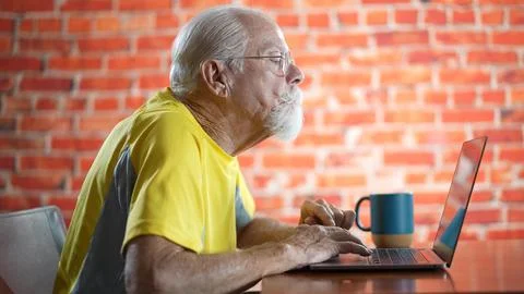 Side view profile of elderly old man sitting at desk using laptop computer Stock Photos