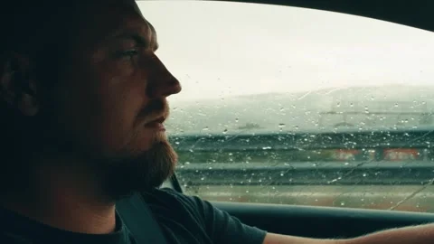 Side view in profile of young white man driving car outside window rainy weather Stock Footage 318602292