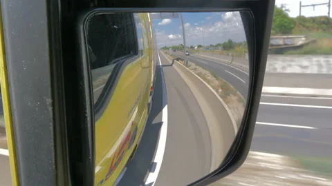 Side view from a rear view mirror of yellow truck rolling on highway Stock Footage 143717740