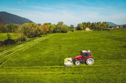 Side view of a red tractor mowing a grass field in the countryside on a sunny Stock Photos