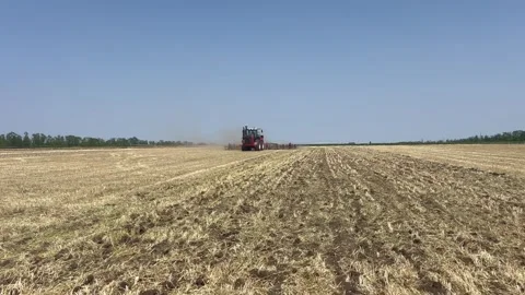 Side view: A red tractor with a trailed cultivator rides across the field in the Stock Footage 317141471