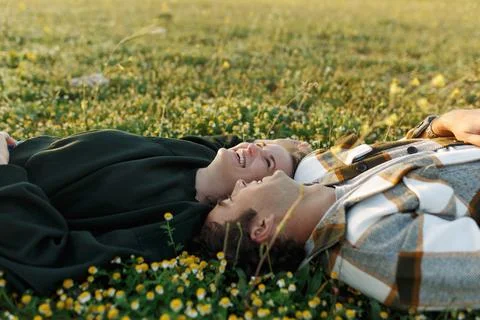 Side view of relaxed young couple lying together on green grass with eyes c.. Stock Photos