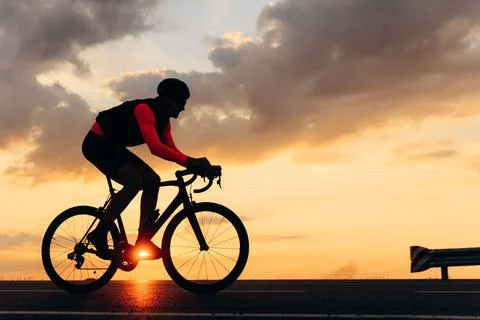 Side view of road cyclist training during amazing sunset Stock Photos