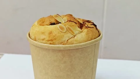 Side view of a round raisin bread with almond flakes in a paper cup. Stock Footage 345815780