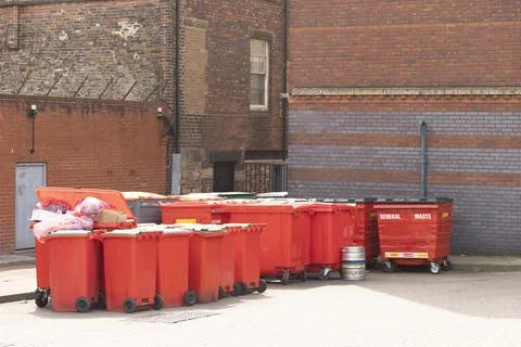Side view on a row of red  recycling bins along a brick wall in a city alley, Stock Photos