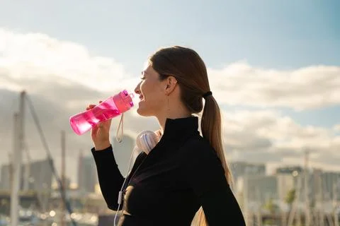 Side view runner girl drinking water from a sports bottle outdoors. Stock Photos