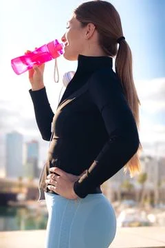 Side view runner girl drinking water from a sports bottle outdoors.Vertical Stock Photos