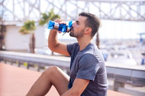 Side view runner man drinking water from a sports bottle outdoors. Stock Photos