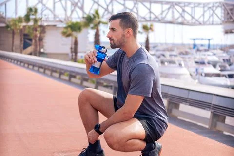 Side view runner man drinking water from a sports bottle outdoors. Stock Photos