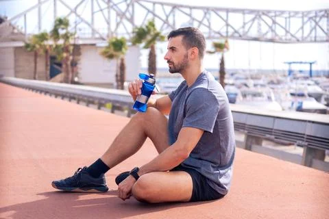 Side view runner man drinking water from a sports bottle outdoors. Stock Photos