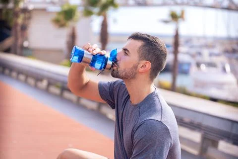 Side view runner man drinking water from a sports bottle outdoors. Stock Photos
