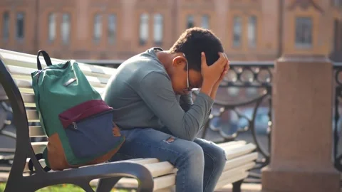 Side view of sad mixed-race schoolboy sitting alone on bench outdoors Stock Footage 141928905