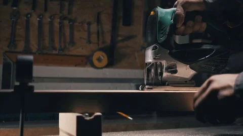 Side view, сarpentry workshop in the background, man with an electric jig saw cu 스톡 동영상 78438255