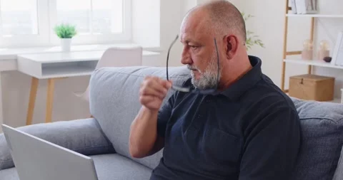 Side view of senior man using laptop on sofa in bright modern living room Stock Footage 327738776
