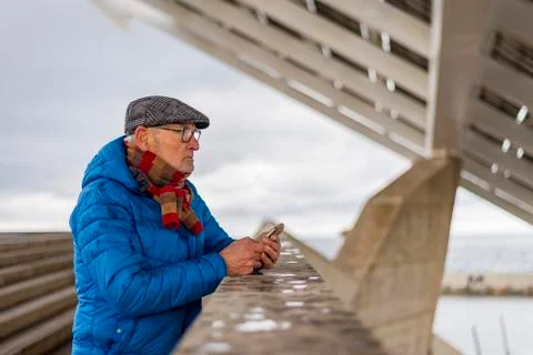 Side view of senior man using smart phone while standing by retaining wall Stock Photos