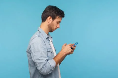Side view of serious man in worker denim shirt texting message in social medi Stock Photos