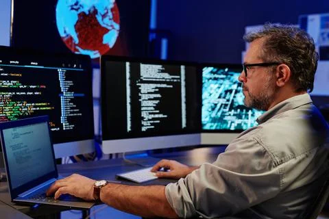 Side view of serious server engineer using laptop and computers Stock Photos