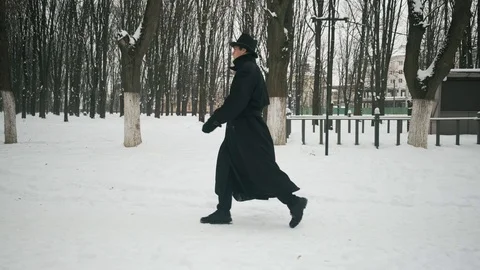 Side view shot: A man in a black cloak and hat walks in the winter park. 60fps Stockbeeldmateriaal 102194876