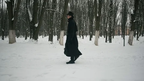 Side view shot: A man in a black cloak and hat walks in the winter park. 60fps Stockbeeldmateriaal 102196616