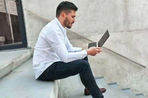 Side view shot of young bearded man sitting on the concrete stairs in urban c Stock Photos