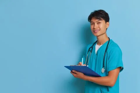 Side view shot of young guy in medical clothes on blue background, making notes Stock Photos