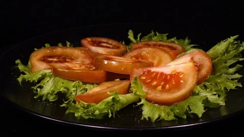 Side view of sliced pink tomato on salad Frillice leaves, put on black plate Stock Footage 74885510