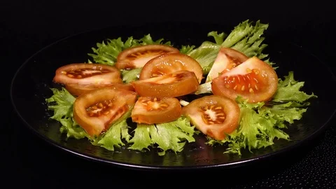 Side view of sliced pink tomato on salad Frillice leaves, put on black plate Stock Footage 74951291