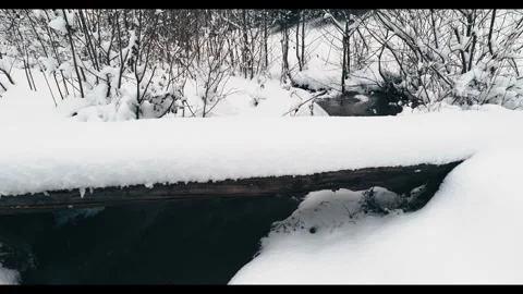 Side view of small wooden bridge covered in deep snow over mountain creek Stock Footage 328410150