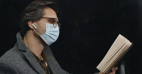 Side view of smart guy in protective mask turning book page while sitting in Stock Footage 148486590