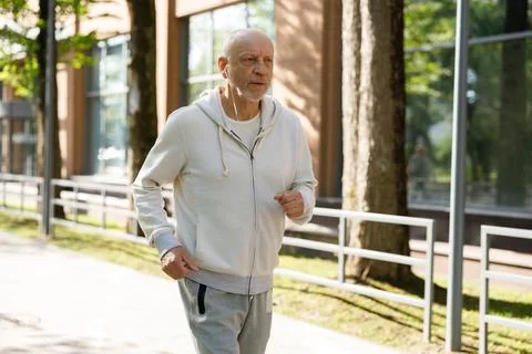 SIDE VIEW OF THE SMILED MATURE MAN RUNNING AND WEARING HEADPHONES IN THE STREET Stock Photos