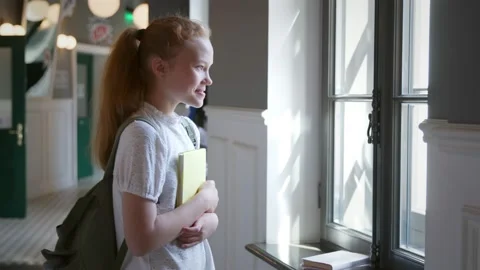 Side view of smiling schoolgirl looking through window in school corridor Vidéo 206691379