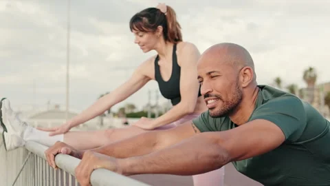 Side view of sportive young couple doing legs warms-up and stretching before Stock Footage 298631646
