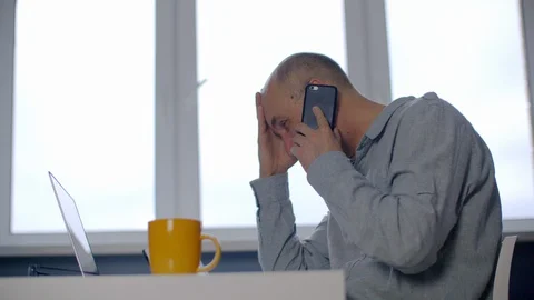 Side view of stressed man talking on smartphone at workplace Stock Footage 129938776
