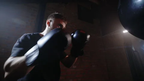 Side view of the strong boxer man hitting the boxing bag wearing black boxing Stock Footage 207206541