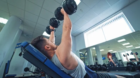 Side view of a strong man with biceps lying on desk and lifting dumbbells in gym Stock Footage 111413855