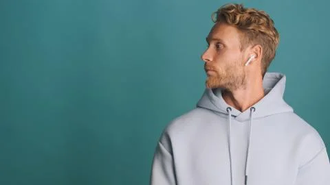 Side view of stylish bearded man in hoodie wear wireless earphones standing near Foto stock