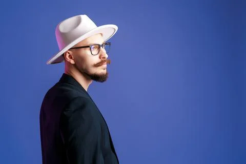 Side view of stylish bearded man in white wide-brimmed hat and blazer who Stock Photos