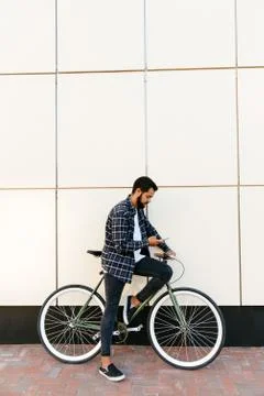 Side view of stylish man sitting on bike with cell phone, outdoors Stock Photos