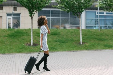 Side view of the stylishly dressed afro-american woman holding the luggage while Stock Photos