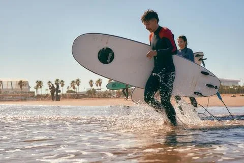 Side view of surfers in wetsuits running into the sea holding surfboards Stock Photos