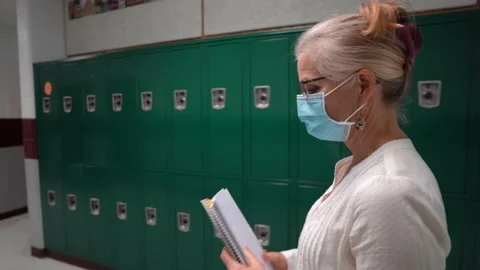Side view of teacher walking down a hallway in an empty school wearing a medical Video stock 137646173